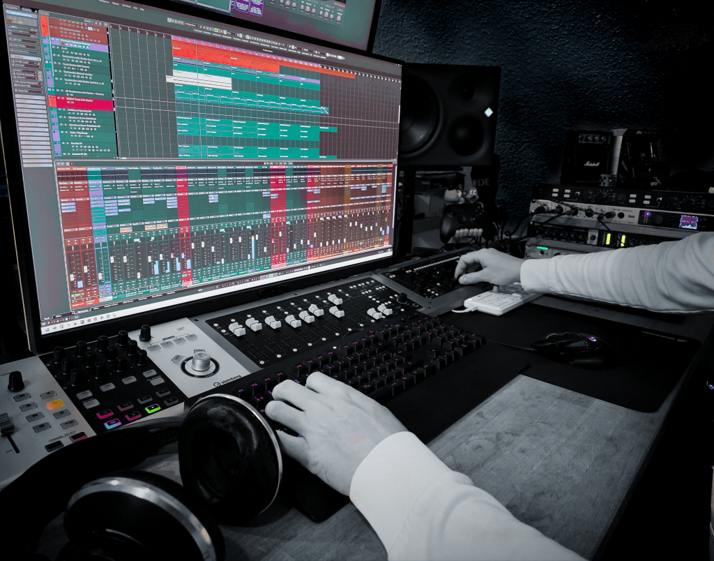 Close-up of a music producer working on a digital audio workstation (DAW) with multitrack recording software on a large monitor, using a MIDI keyboard and mixing controller in a professional home music studio setup with speakers and headphones.